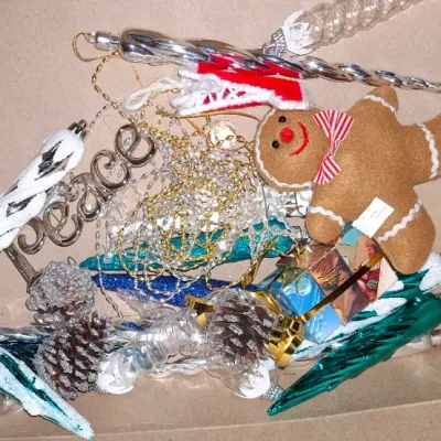 Sale Photo Thumbnail #188: Cardboard box filled with assorted vintage and modern Christmas ornaments, including silver icicles, a plush gingerbread man, beaded garlands, and pinecone accents.