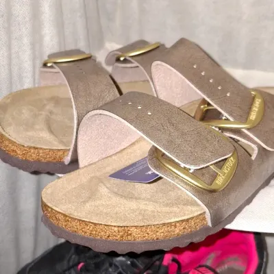 Pair of metallic brown Birkenstock Arizona Big Buckle sandals sitting above a pair of black and pink Nike athletic sneakers.