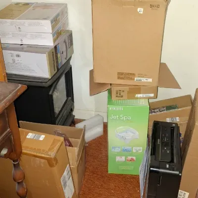 Collection of boxed household items, including a HoMedics Jet Spa footbath, an IKEA box, shipping cartons, and a black electronic printer...