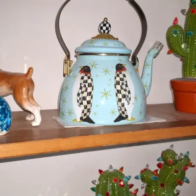 Sale Photo Thumbnail #273: Collection of shelf decor including a MacKenzie-Childs light blue penguin tea kettle, a porcelain boxer dog figurine, ceramic cactus holiday trees, and blue art glass pieces.