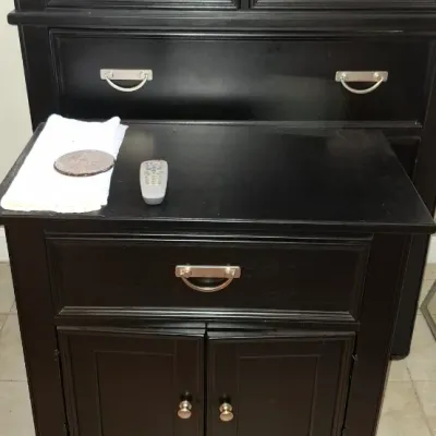 Sale Photo Thumbnail #220: Black painted wooden nightstand with one drawer and two doors featuring silver bail handles, positioned in front of a matching tall dresser.