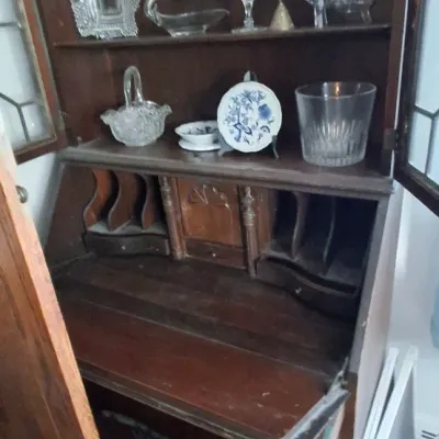 Sale Photo Thumbnail #241: Vintage dark wood secretary desk with leaded glass door hutch, featuring interior cubbies and display shelves filled with pressed glass decor.
