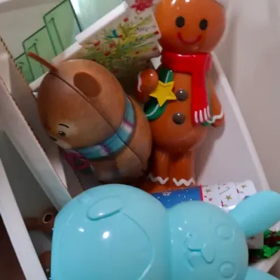 Plastic white bin filled with small holiday items and toys, including a gingerbread man figure, a blue rabbit toy, and a small brown...