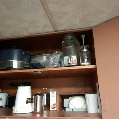 Selection of small kitchen appliances and glassware stored in a cabinet, including a rice cooker, popcorn maker, electric roaster, and...