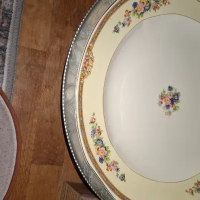 Sale Photo Thumbnail #271: Vintage ceramic serving platter featuring a cream rim with colorful floral sprigs, set inside an ornate silver-plated frame, shown alongside a simple stoneware dish.