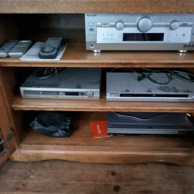 Sale Photo Thumbnail #251: Wooden media cabinet filled with vintage home audio and video equipment, including an AV receiver, DVD players, and remote controls.