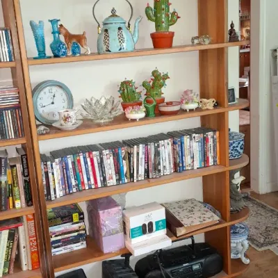 Sale Photo Thumbnail #276: Tall light wood bookshelf holding a variety of decorative glassware, figurines, books, DVDs, and electronics, including a vintage Sony boombox.