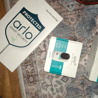 Sale Photo Thumbnail #265: Selection of Arlo smart home security devices in original boxes, including an indoor/outdoor pan-tilt camera, an Essential security camera set, and a security yard sign.