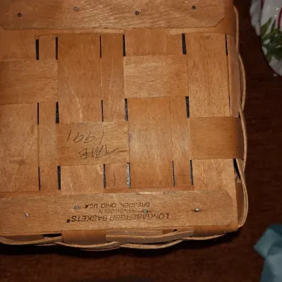 Underside of a 1991 handwoven Longaberger woven wood basket, featuring the maker's burn stamp and weaver's initials.