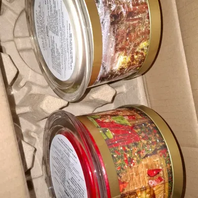 Two Homeworx by Harry Slatkin holiday-themed 4-wick scented candles with glass lids, packed in their original shipping box insert.