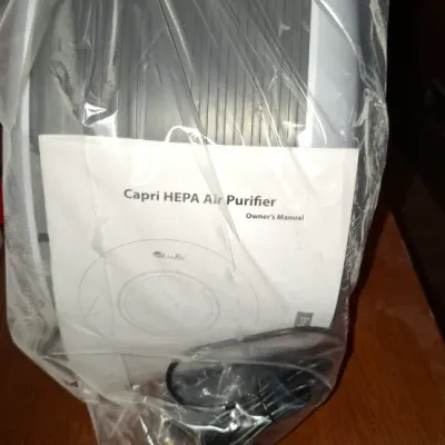 Capri HEPA air purifier packaged in a clear plastic bag with its owner's manual and power cord.