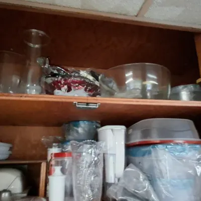 Assorted glassware, plastic storage containers, and kitchenware stored inside a wooden cabinet.