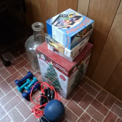 Collection of household items including boxed games, a Nostalgic Christmas Tree box, small fitness dumbbells, a medicine ball, and a...