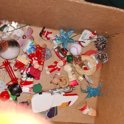Sale Photo Thumbnail #175: Cardboard box filled with an assortment of vintage and modern Christmas ornaments, including miniature figures, pinecones, and decorative baubles.