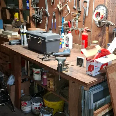 Sale Photo Thumbnail #236: Rustic wooden workbench fully stocked with a table vise, toolbox, power tools, paint cans, and an assortment of hand tools hanging from pegboard.