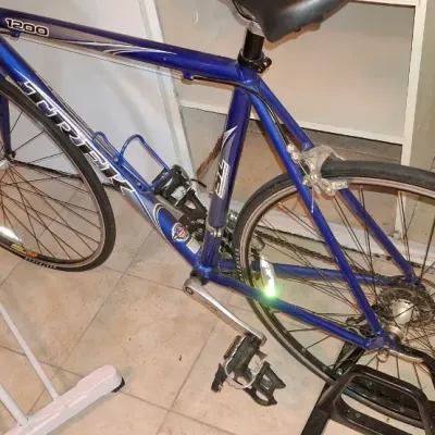 Sale Photo Thumbnail #218: Trek 1200 SL road bike featuring a metallic blue aluminum frame, drop handlebars, and mounted on an indoor training stand.