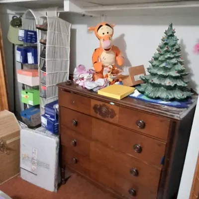Vintage wooden four-drawer chest holding a ceramic Christmas tree, plush Tigger toy, and various household goods.