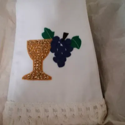 Handmade white ceremonial fabric banner or towel, featuring felt and sequin appliqués of a chalice and grapes with a crocheted fringe...