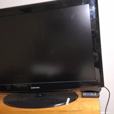 Sale Photo Thumbnail #207: Black Samsung flat-screen television on an oval base stand, displayed on a wooden surface with a remote.