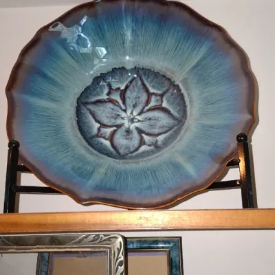 Sale Photo Thumbnail #275: Large decorative studio pottery bowl featuring a scalloped edge and a blue glaze with a central floral motif, displayed on a metal stand.