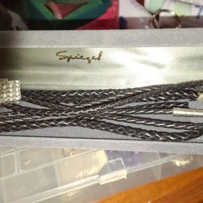 Vintage rhinestone-embellished bolo tie with black braided cord, housed in an original grey velvet Spiegel presentation box.