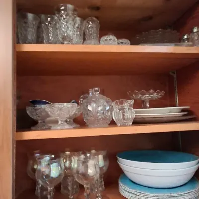 Wooden cabinet filled with vintage glassware, pressed glass serveware, clear stemware, and modern turquoise and white ceramic dinnerware.