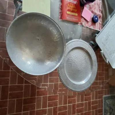 Collection of hammered aluminum serving pieces, including a large bowl, charger plate, and handles tray, displaying visible surface...
