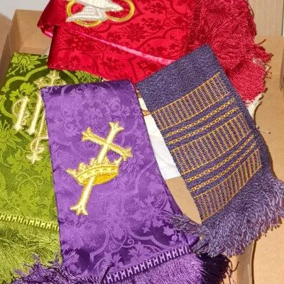 Collection of embroidered clerical stoles in various liturgical colors, including red, green, and purple damask fabrics with fringe trim.