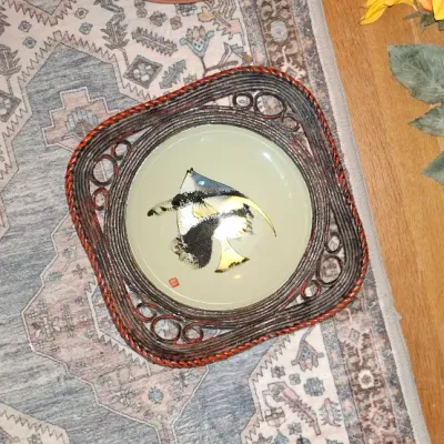 Sale Photo Thumbnail #270: Vintage Asian ceramic decorative plate featuring an angelfish design, framed within an ornate square woven wicker display holder.