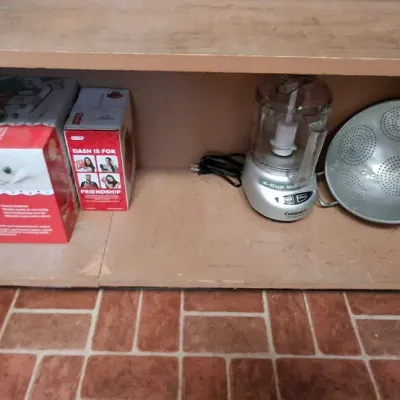 Selection of kitchen items inside a wooden cabinet, including boxed appliance sets, a Cuisinart 4-cup mini food processor, and a...
