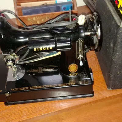 Sale Photo Thumbnail #180: Vintage Singer Featherweight 221 portable sewing machine in black enamel with gold decals, complete with its original carrying case.