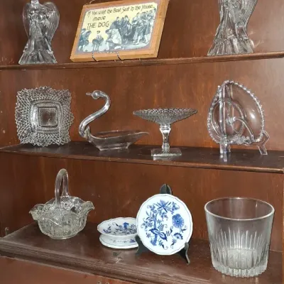 Sale Photo Thumbnail #243: Wooden secretary hutch filled with decorative collectibles, including cut glass serving pieces, crystal angel figurines, and blue and white porcelain butter chips.