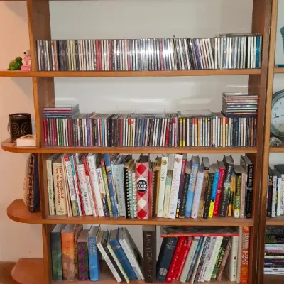 Sale Photo Thumbnail #277: Tall mid-century wooden bookcase filled with CDs, hardback and paperback books, and decorative accents.