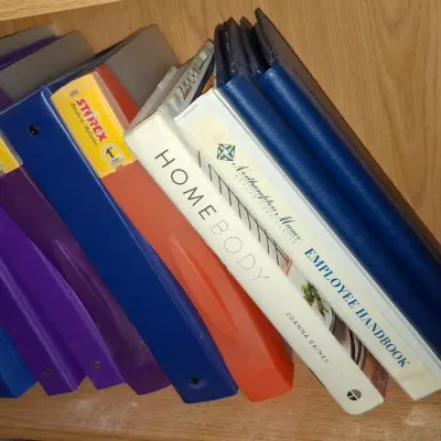 Collection of three-ring binders, employee handbooks, and reference books, including Joanna Gaines' 'Homebody,' stored on...