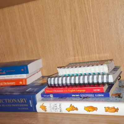 Assortment of reference books, spiral notebooks, and a copy of 'The People Called Apache' resting on a wooden shelf.