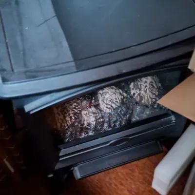 Black electric fireplace heater unit featuring a glass front panel filled with decorative pinecones.