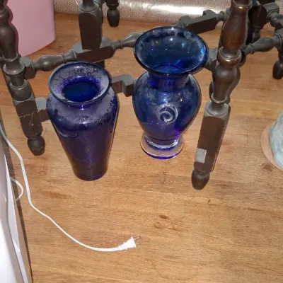 Sale Photo Thumbnail #257: Pair of cobalt blue glass vases resting under a dark wood accent table, showing light surface dust.
