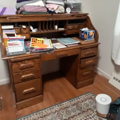 Sale Photo Thumbnail #115: Vintage oak roll-top desk with carved drawer fronts and multiple compartments, topped with various household items.