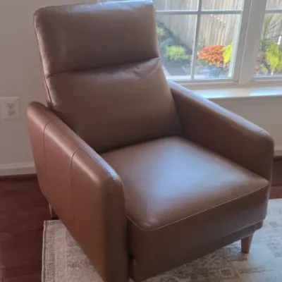 Sale Photo Thumbnail #8: Contemporary brown leather accent armchair with tapered wooden legs, shown positioned on a patterned area rug next to a window.