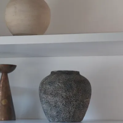 Sale Photo Thumbnail #28: Collection of decorative items including a pair of brass conical candle holders, a textured dark ceramic vase, and a beige spherical vase displayed on white floating shelves.