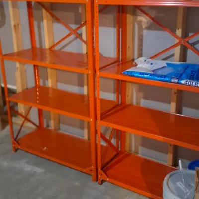 Sale Photo Thumbnail #67: Pair of heavy-duty orange steel shelving units with five tiers each, set up against exposed wall studs in a basement.