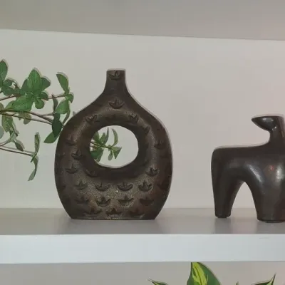 Sale Photo Thumbnail #21: Trio of shelf decorative objects including a potted green plant, a dark textured donut vase, and a stylized mid-century ceramic animal figurine.