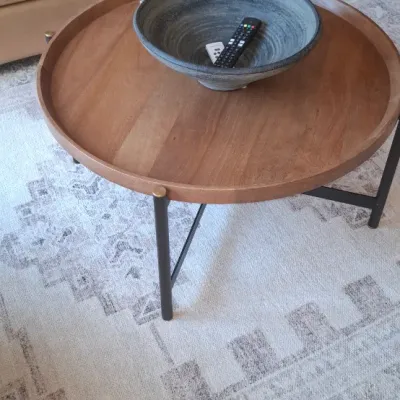 Sale Photo Thumbnail #6: Contemporary round wooden coffee table with a tray top design and black metal legs, set on a distressed neutral area rug.