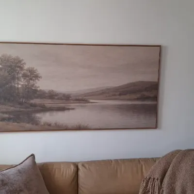 Sale Photo Thumbnail #33: Large panoramic landscape wall art featuring a serene lake scene in muted neutral tones, set in a thin wooden frame above a tan sofa.