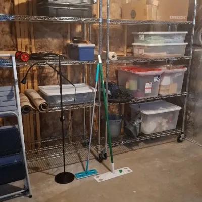 Sale Photo Thumbnail #65: Two tall wire shelving units holding various storage totes, luggage, and household goods, flanked by cleaning mops and step ladders.
