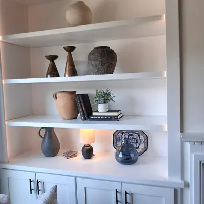 Sale Photo Thumbnail #16: Custom white built-in shelving unit featuring integrated accent lighting and lower storage cabinets with modern black hardware, styled with contemporary ceramic vessels, books, and decorative accents.