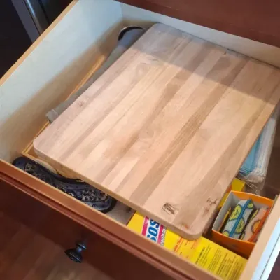 Sale Photo Thumbnail #76: Open kitchen drawer containing a wood butcher-block cutting board and various household cleaning supplies.