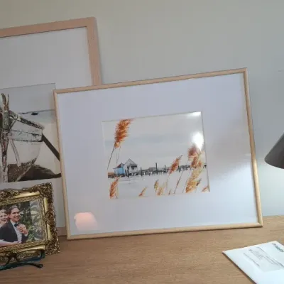 Sale Photo Thumbnail #36: Modern table arrangement featuring light wood framed coastal prints, an ornate gold photo frame, a candle, potted plant, and a rounded metallic mushroom-style table lamp.