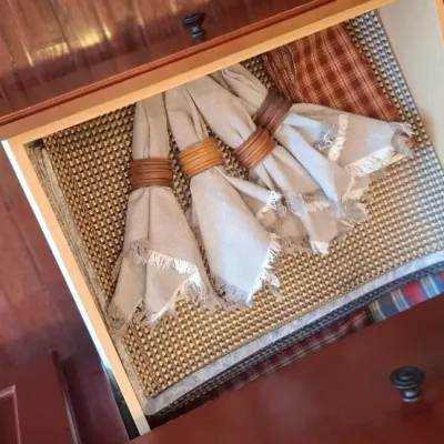 Sale Photo Thumbnail #77: Open wooden cabinet drawer filled with cloth table linens, woven placemats, and napkins held by wooden ring holders.