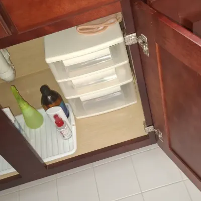 Sale Photo Thumbnail #82: Under-sink storage cabinet featuring clear plastic three-drawer organizers and various cleaning bottles.